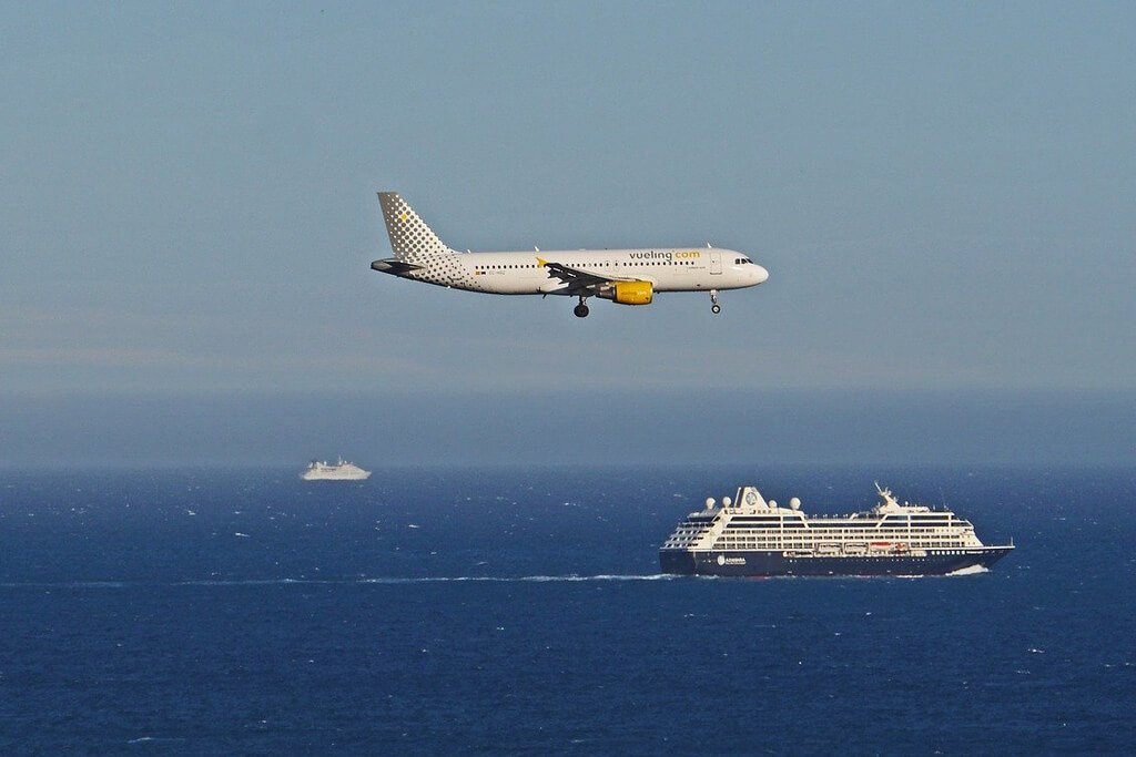 Airplane flying over ocean with cruise ship
